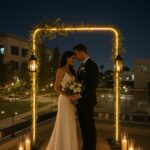 Bride and groom share an intimate moment under a softly lit wedding arch on the balcony at night.