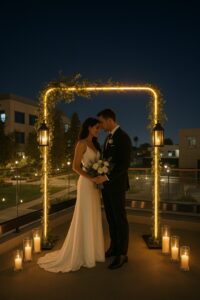 Bride and groom share an intimate moment under a softly lit wedding arch on the balcony at night.
